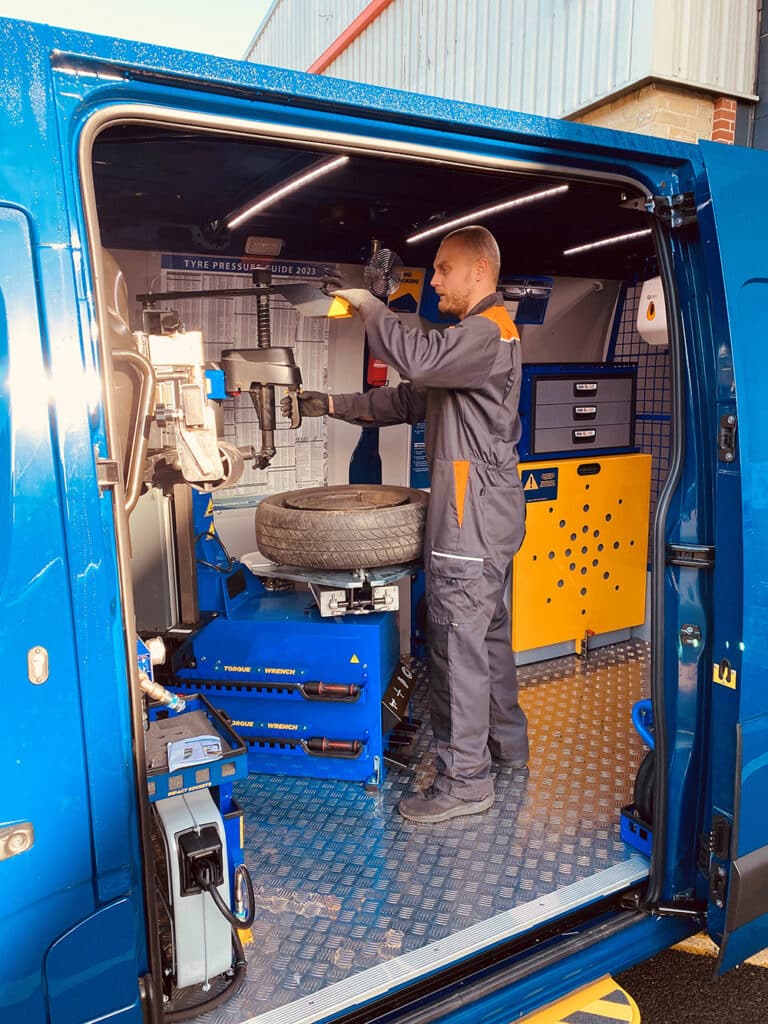 Man installing a new tyre to a wheel inside a blue mobile workshop